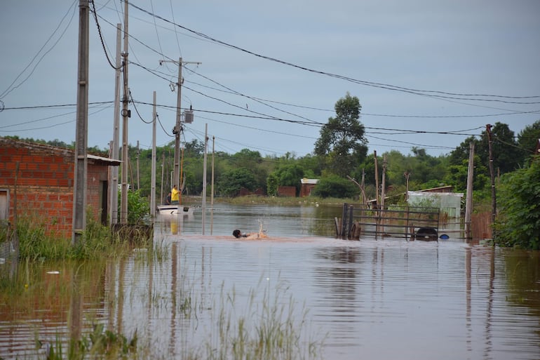 Los niños jugando en el agua y un técnico de ANDE intentando desconectar el fluido eléctrico en el barrio.