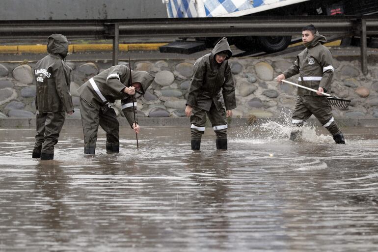 Personal de Carabineros trabaja en calles inundadas por la lluvia este jueves, en Santiago (Chile). Decenas de miles de personas se han visto damnificadas por las intensas lluvias torrenciales que azotan desde el martes la región central del país y que desde esta madrugada caen con fuerza en la capital, Santiago de Chile, donde ya han causado desalojos por inundación, interrupciones del suministro de electricidad y problemas de tránsito y han obligado a suspender las clases en los colegios y universidades.