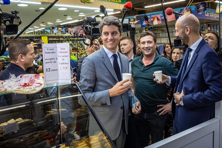 El primer Ministro francés Gabriel Attal (centro) visita un mercado de alimentos con el candidato del partido mayoritario presidencial 'ÄòRenaissance'Äô, Stanislas Guerini (derecha), como parte de la campaña de segunda vuelta de las elecciones legislativas en París.