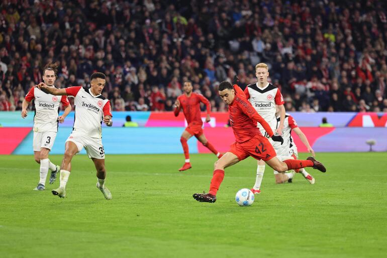 Bayern Munich's German midfielder #42 Jamal Musiala (end R) kicks the ball to score the 3-0 goal during the German first division Bundesliga football match between FC Bayern Munich and Eintracht Frankfurt in Munich, southern Germany on February 23, 2025. (Photo by Alexandra BEIER / AFP) / DFL REGULATIONS PROHIBIT ANY USE OF PHOTOGRAPHS AS IMAGE SEQUENCES AND/OR QUASI-VIDEO