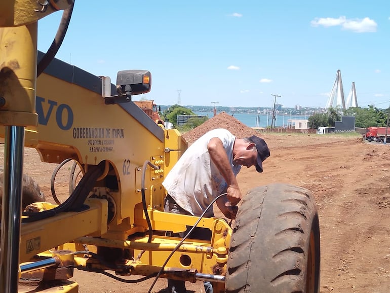 Un operario en tareas de mantenimiento a una máquina vial de la Gobernación. Al fondo el majestuoso puente internacional "San Roque González de Santa Cruz", que une con Posadas, Argentina.