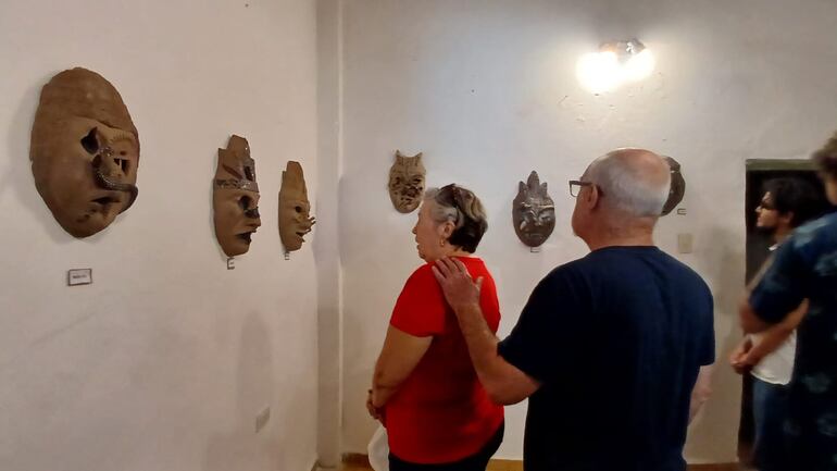 personas observando máscaras hechas de cerámica en una galería de arte en Aregua