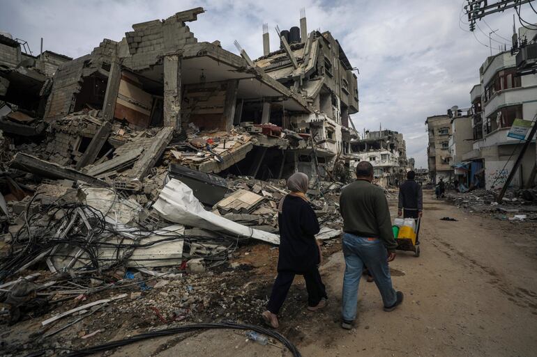 Varias personas pasan junto a edificios destruidos por bombardeos israelíes en el sur de la Franja de Gaza, el martes.