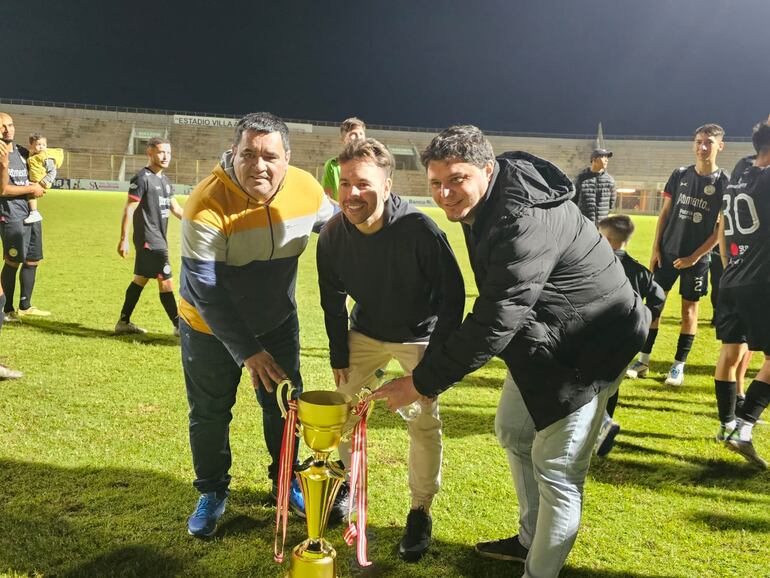 El presidente del club Deportivo Itapuense, Guillermo Ojeda (centro) con Florencio Ferreira y Tomás García, con la flamante copa de campeón 2023 conquistado en el coqueto estadio “Villa Alegre” de la Liga Encarnacena de Fútbol.