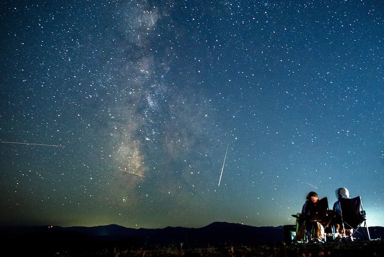 Una pareja observa cómo un meteoro surca el cielo nocturno más allá de la Vía Láctea durante la lluvia de meteoros de las Perseidas sobre el lago Kozjak, a unos 45 km de la capital Skopje (Macedonia del Norte).