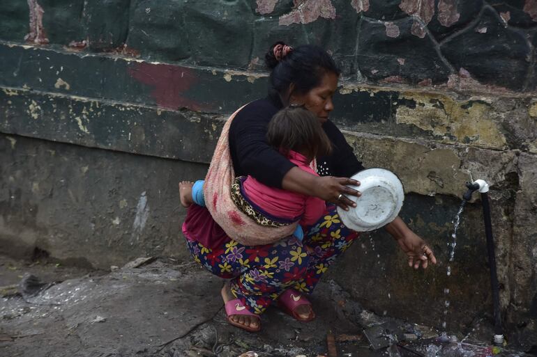 Indígena lava un plato en la precaria vereda de la Intendencia Militar, que se encuentra llena de agua servida, sobre la avenida Artigas.