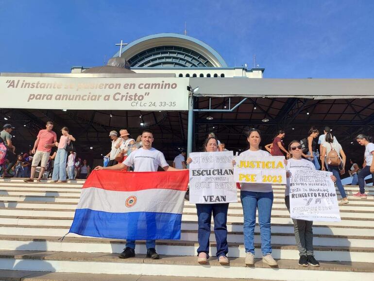 Exfuncionarios de Itaipú se llegaron a la Basílica con carteles pidiendo una respuesta del presidente de la República.