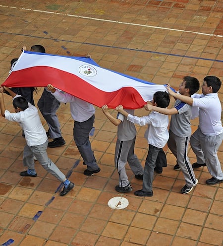 Niños de una escuela llevan en alto una bandera paraguaya. Foto del Observatorio Educativo Ciudadano.