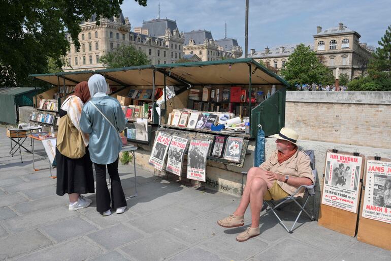 Un librero de 65 años sentado en su puesto, vendiendo libros antiguos y carteles antiguos, en la orilla izquierda del río Sena en París.