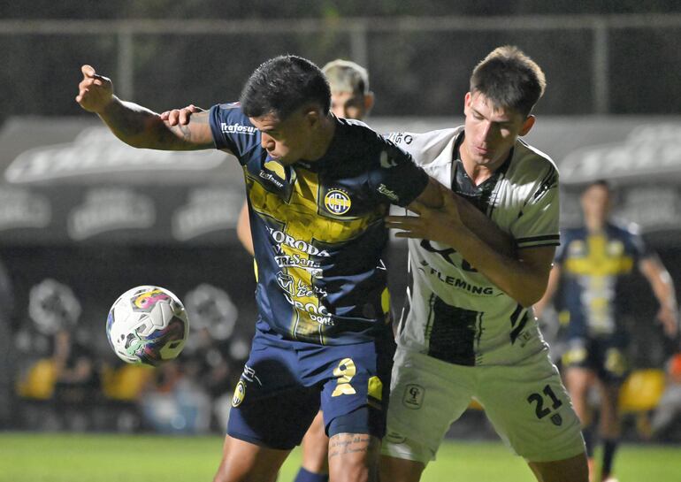 El delantero de Trinidad, Óscar Giménez, cubre con el cuerpo la tenencia de la pelota ante la presión de Lucas Romero.