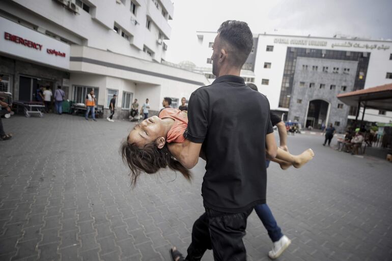 Un hombre lleva en brazos a una niña herida, fuera del hospital Al-Shifa en la Ciudad de Gaza, que fue golpeada con más de 500 ataques aéreos por parte de Israel durante la noche del domingo y madrugada del lunes.