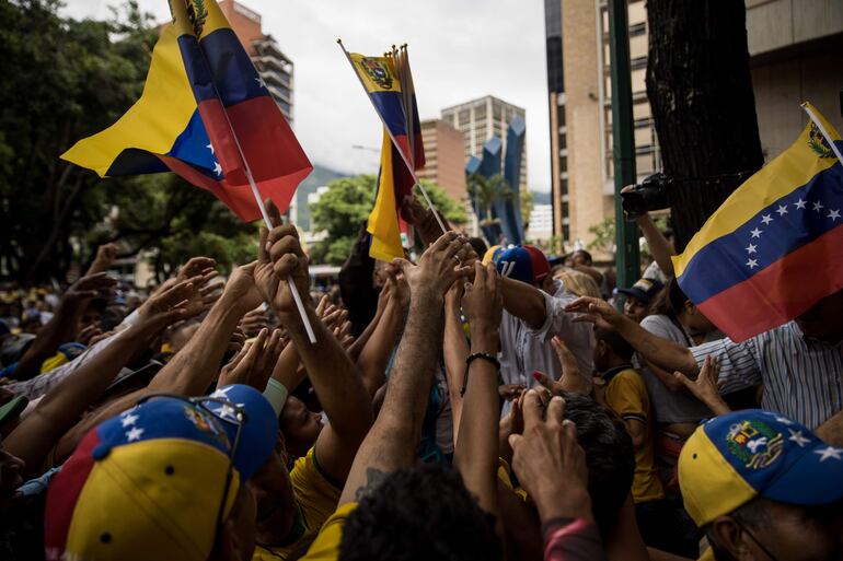 Fotografía de archivo fechada el 24 de junio del 2023 personas mientras sostienen banderas de Venezuela en un acto político, en Caracas (Venezuela). Las instituciones, el Gobierno, la oposición y el pueblo de Venezuela están calentando el escenario político de cara a las primarias que el antichavismo celebrará el 22 de octubre, un hito hacia el que el país camina entre discursos altisonantes y amenazas que van recrudeciéndose, cuando todavía faltan 100 días para la cita. EFE/ Miguel Gutierrez.