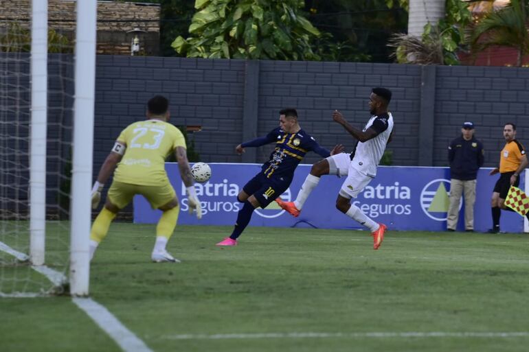 Alex Álvarez, de Trinidense, ante la marca del jugador de Tacuary, Paulo Lima, con Gaspar Servio en el arco.