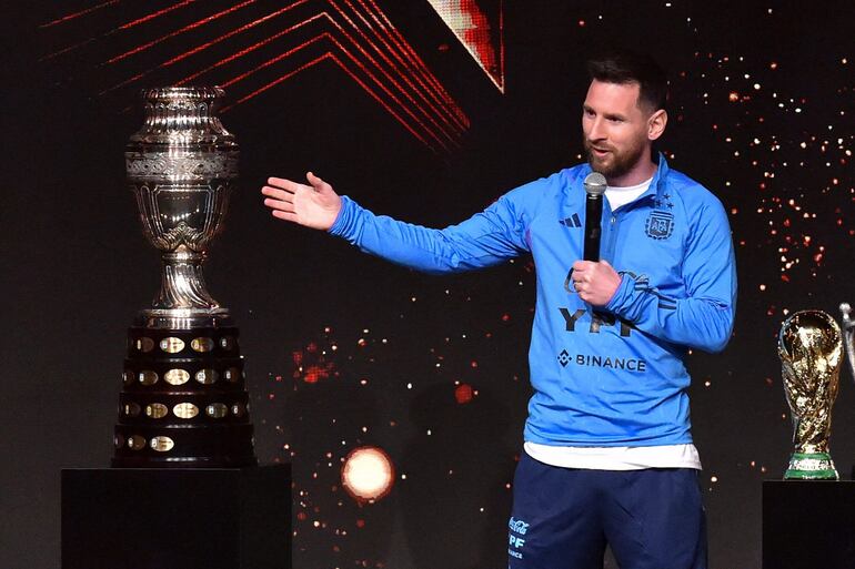 El delantero argentino Lionel Messi pronuncia un discurso entre el trofeo de la Copa América (izq.) y una réplica del Mundial, durante un homenaje de la Conmebol a los integrantes de la selección argentina por ganar el Mundial de Qatar 2022.