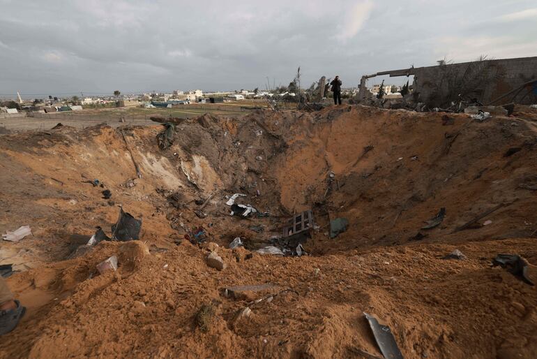 Un palestino se para junto a un gran agujero en la tierra en Rafah luego de un ataque aéreo israelí a la franja de Gaza.