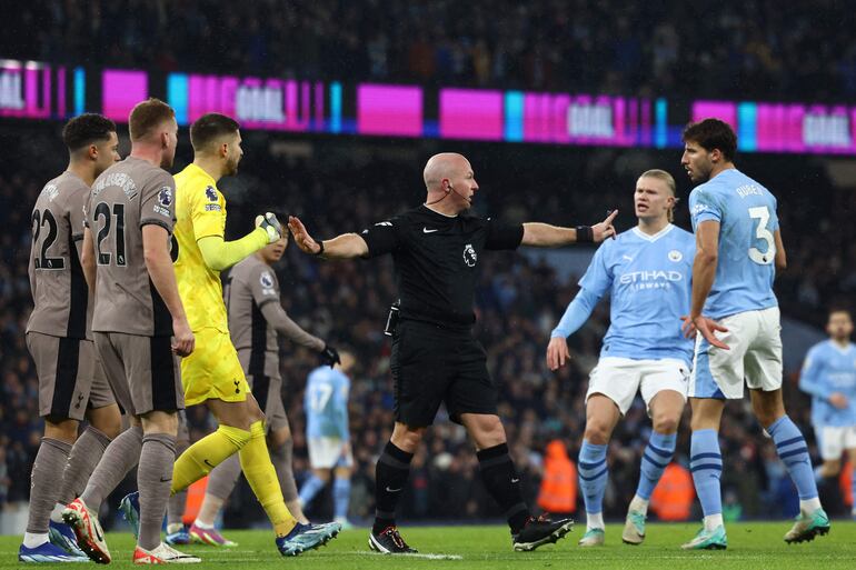 El árbitro inglés Simon Hooper (C) está rodeado de jugadores durante el partido de fútbol de la Premier League inglesa entre Manchester City y Tottenham Hotspur en el estadio Etihad de Manchester, noroeste de Inglaterra, el 3 de diciembre de 2023.