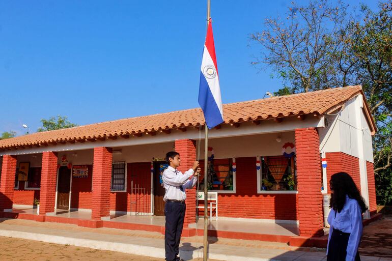 Alumnos izan la bandera paraguaya durante la habilitación de mejoras en la escuela Curuzú Francisco de Villarrica.