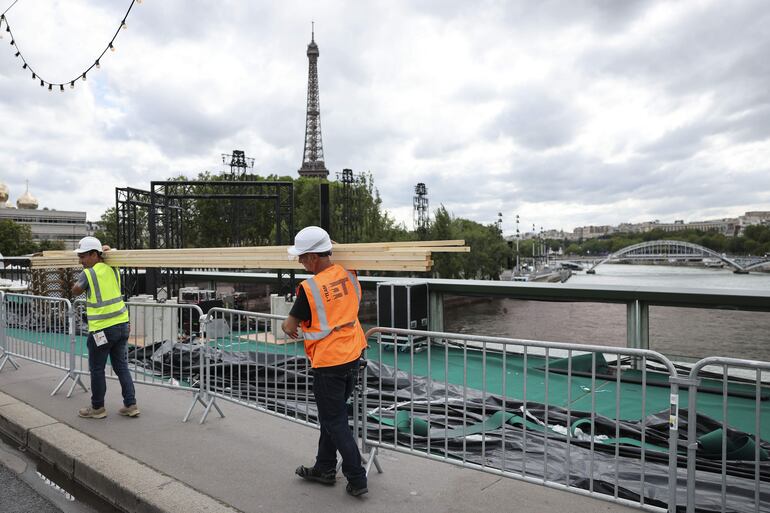  Varios operarios pasan ante el río Sena de París. Será el escenario elegido para la ceremonia de inauguración de los Juegos Olímpicos el próximo viernes 26 de Julio.  
