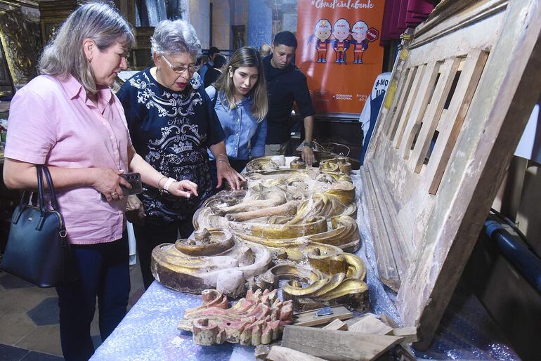 Personas observan las piezas del otro retablo que también está siendo restaurado en la Iglesia de la Santísima Trinidad, a cargo del MOPC.