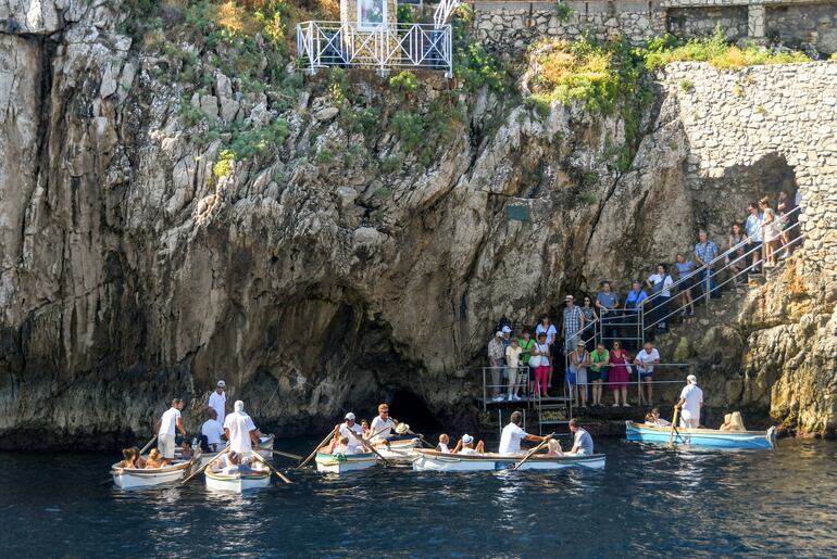 Turistas visitan la Gruta Azul en Capri, Italia. La pequeñísima entrada se observa detrás de los botes.