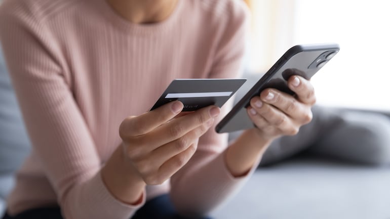 Una mujer revisa su tarjeta de crédito para realizar compras en línea en su teléfono celular.