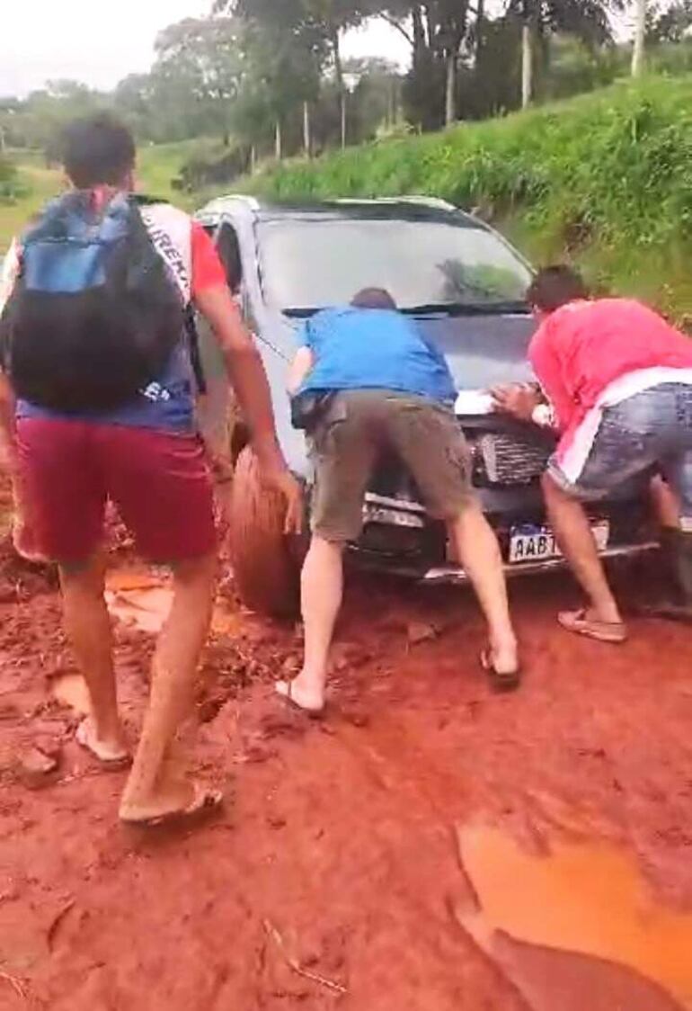 Vecinos tratan de ayudar haciendo fuerza para que salga de la zona fangosa un automóvil en la compañía Costa Báez de Acahay.