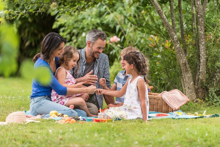 Una familia celebra un picnic sentada sobre un mantel en el pasto, al aire libre.