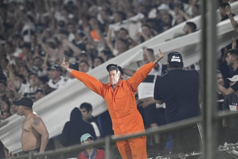 Un hincha de Olimpia disfrazado con un mameluco de color anaranjado (similar al que usan algunos prisioneros en las cárceles de Estados unidos) gesticula desde las gradas, con una careta del expresidente Horacio Cartes. 