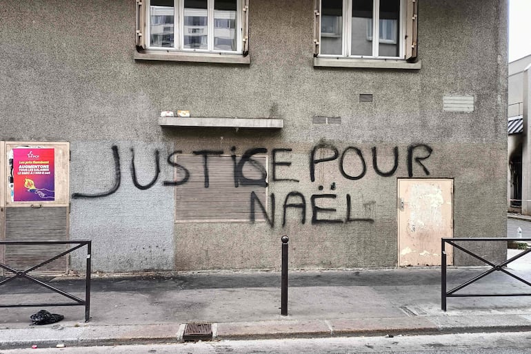 Un letrero que dice "Justicia para Nahel", en una casa al lado del edificio parcialmente incendiado (extremo derecho) de la Brigada de Asistencia para Personas sin Hogar (BAPSA) en París, luego de disturbios dos días después de un La policía le disparó a quemarropa a un niño de 17 años en el pecho en Nanterre, un suburbio al oeste de París.