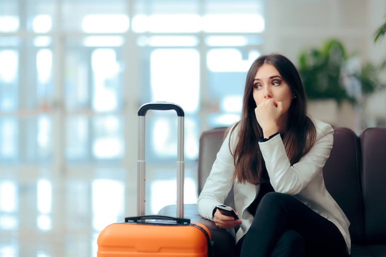 Viajera con su maleta en un aeropuerto mostrando signos de preocupación y nerviosismo.