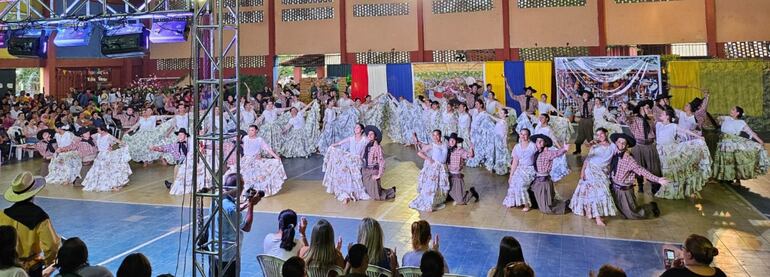 coreografía tradicional con trajes típicos, enmarcados en un colorido escenario decorado con los colores patrios.