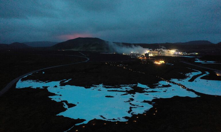 El brillo rojo del magma se ve saliendo del volcán Fagradalsfjall en erupción detrás de la marca turística Blue Lagoon, cerca de la ciudad de Grindavik.