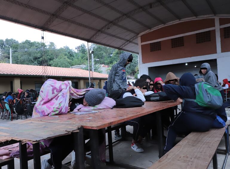 Los estudiantes se refugian bajo una frazada para aguantar el frío intenso, debajo del tinglado en el que estudian, con muebles ya derruidos, en la escuela y colegio Clara Piacentini.