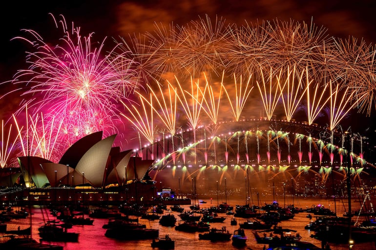 Los fuegos artificiales explotan sobre el puente del puerto de Sídney y la Ópera de Sídney (izq.) durante las celebraciones de Nochevieja en Sídney el 1 de enero de 2024. (Foto de Izhar KHAN / AFP)