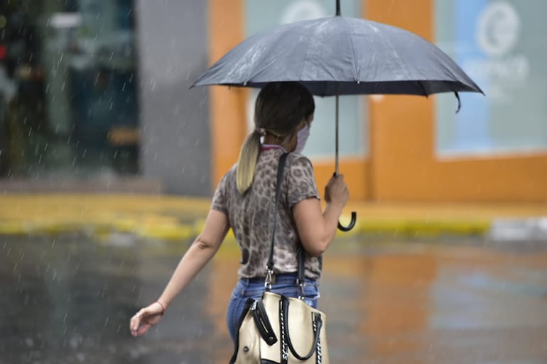 Bajo la lluvia, con paraguas, una mujer cruza la calle.