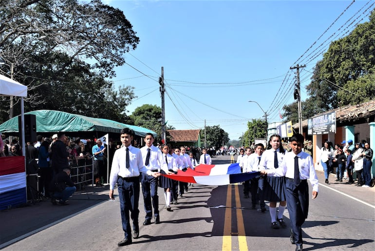 Estudiantes marchan con una bandera paraguaya sobre la ruta PY01.