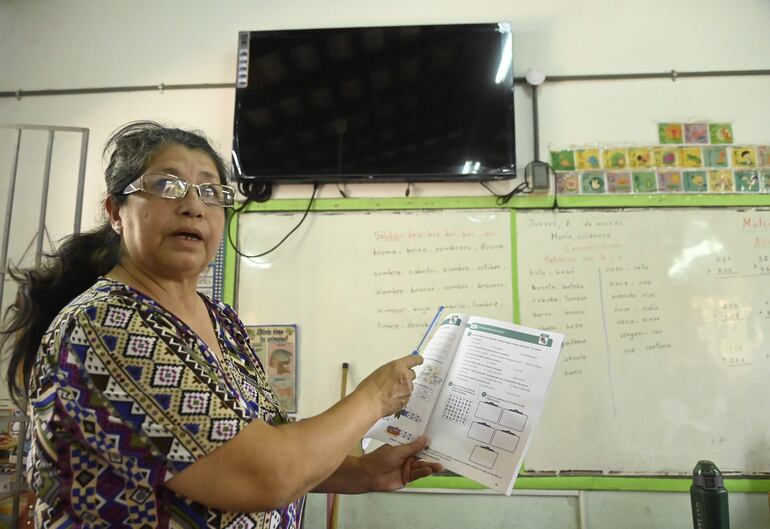 La profesora Antolina Serra de la escuela Roberto L. Petit muestra un libro del programa de Jornada Extendida. El televisor que se observa detrás no cuenta con conexión a internet.