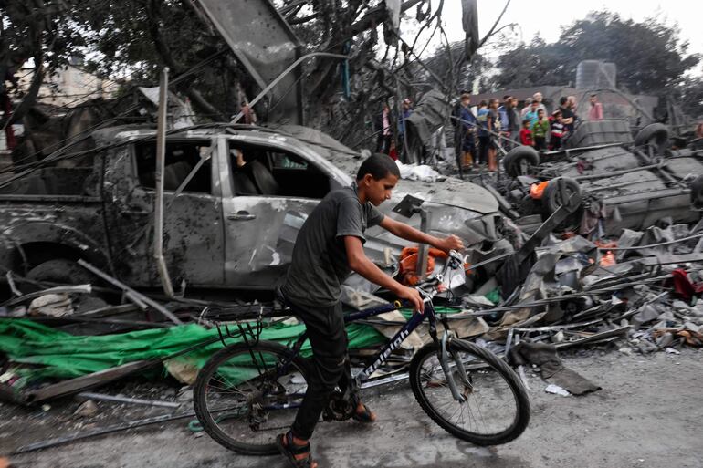 Un joven circula en bicicleta junto a un vehículo destruído y escombros luego de un ataque aéreo israelí sobre el campo de refugiados de Rafah, en el sur de la Franja de Gaza, este miércoles.