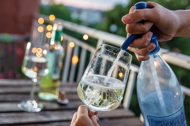 Una persona carga soda de un sifón en una copa con vino blanco.