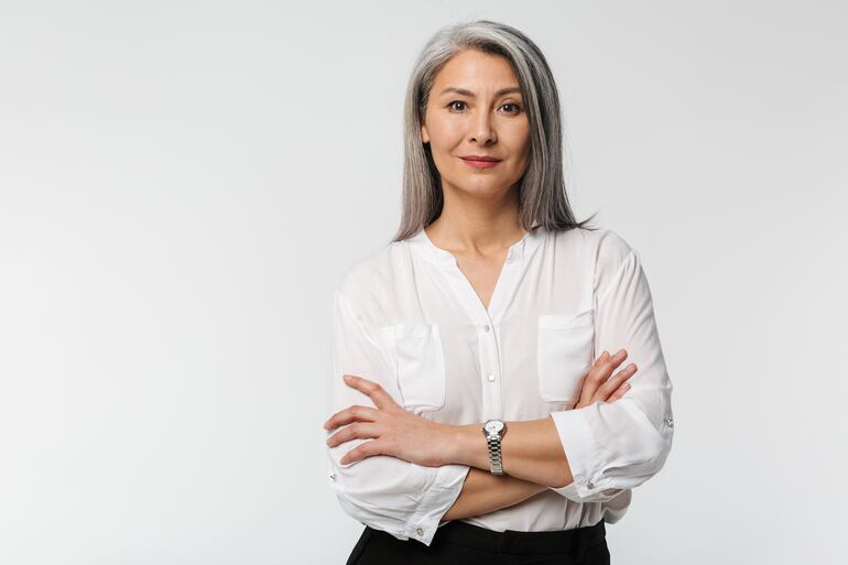 Mujer con canas y pelo largo de brazos cruzados.