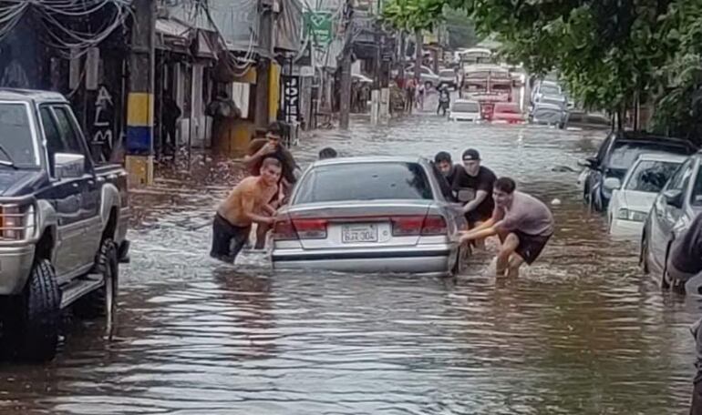 Personas empujando un auto durante las inundaciones en Luque.