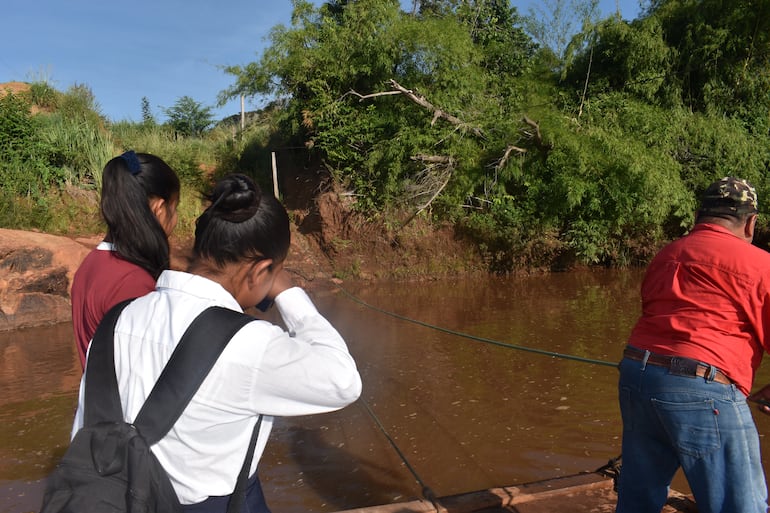 Dos estudiantes realizan la peligrosa travesía en balsa con ayuda del líner de la comunidad para cruzar el río Aquidaban.