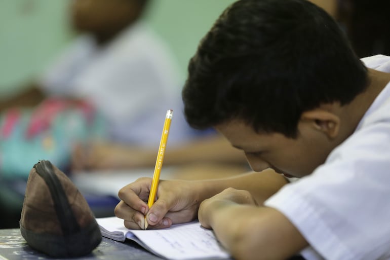 Estudiante escribiendo su lección en una sala de clase. Imagen referencial.