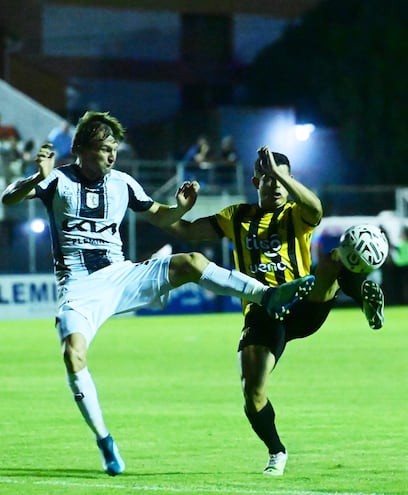 Walter Clar y Mathías Martínez van con pierna levantada para intentar quedarse con el control del balón.