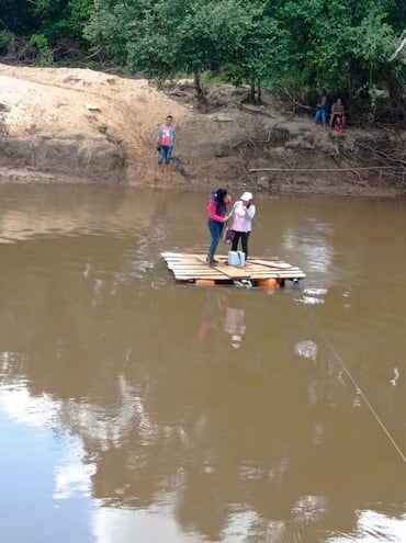 Dos personas cruzan el rio Tebicuary sobre la precaria balsa en Valle-í.