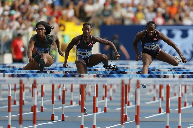 Ackera Nugent (c) se adelanta  con gran velocidad para ganar la prueba de los 100 m con vallas.