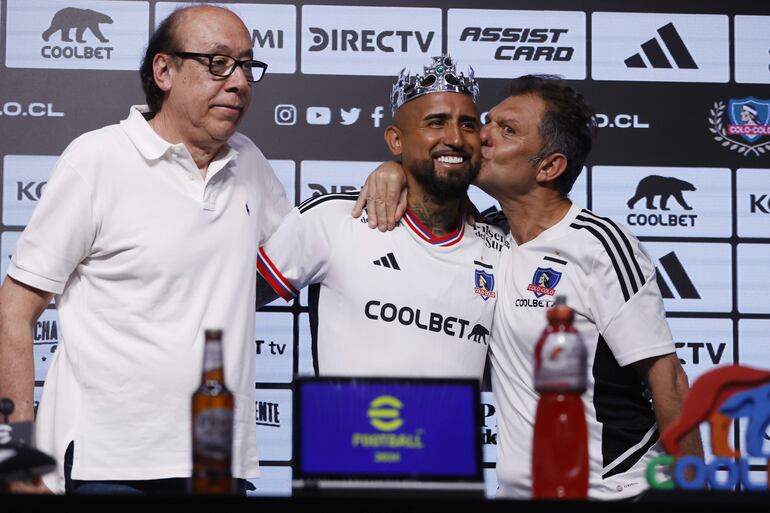 AME1610. SANTIAGO (CHILE), 23/01/2024.- Aníbal Mosa (d), director de Blanco y Negro, concesionaria que administra al Colo Colo, besa en la mejilla al chileno Arturo Vidal (c), acompañados del presidente deportivo de Colo Colo, Alfredo Stöhwing (d), durante la presentación de Vidal como nuevo jugador del equipo, hoy, en Santiago (Chile). Vidal retorna al club que le vio nacer como el fichaje más caro de Colo Colo en los últimos tiempos, como agente libre tras finalizar su vínculo en diciembre pasado con el brasileño Atlético Paranaense y según la prensa y el propio jugador, "por amor al equipo" habiendo rechazado ofertas económicas más jugosas de otras ligas, como la colombiana. EFE/ Elvis González
