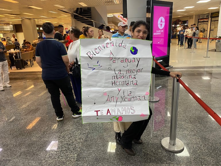 María Belén Martínez sostiene un cartel hecho a mano para recibir a su madrina, hermana y tía, celebrando su llegada a Paraguay.