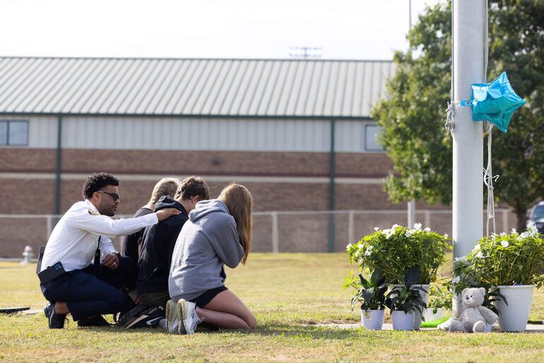 El capellán del estado de Georgia, Ronald Clark, consuela a los estudiantes mientras se arrodillan frente a un monumento improvisado en la escuela secundaria Apalachee el 5 de septiembre de 2024 en Winder, Georgia. 