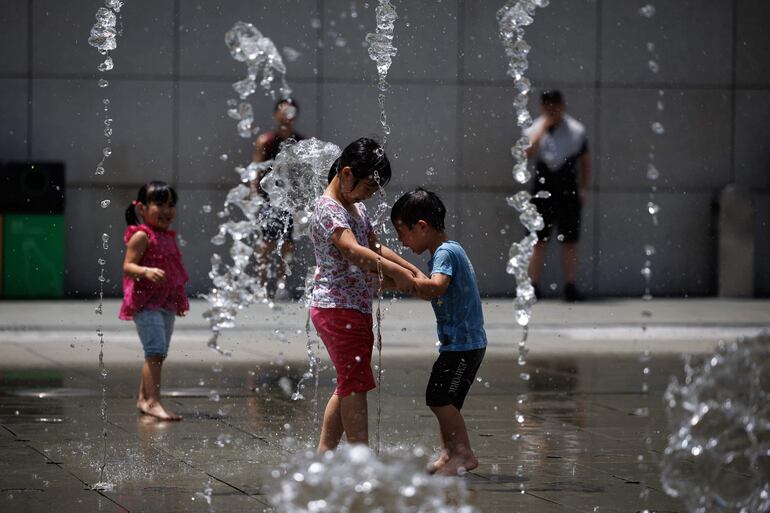 Un grupo de niños chinos se refresca en una fuente en China.